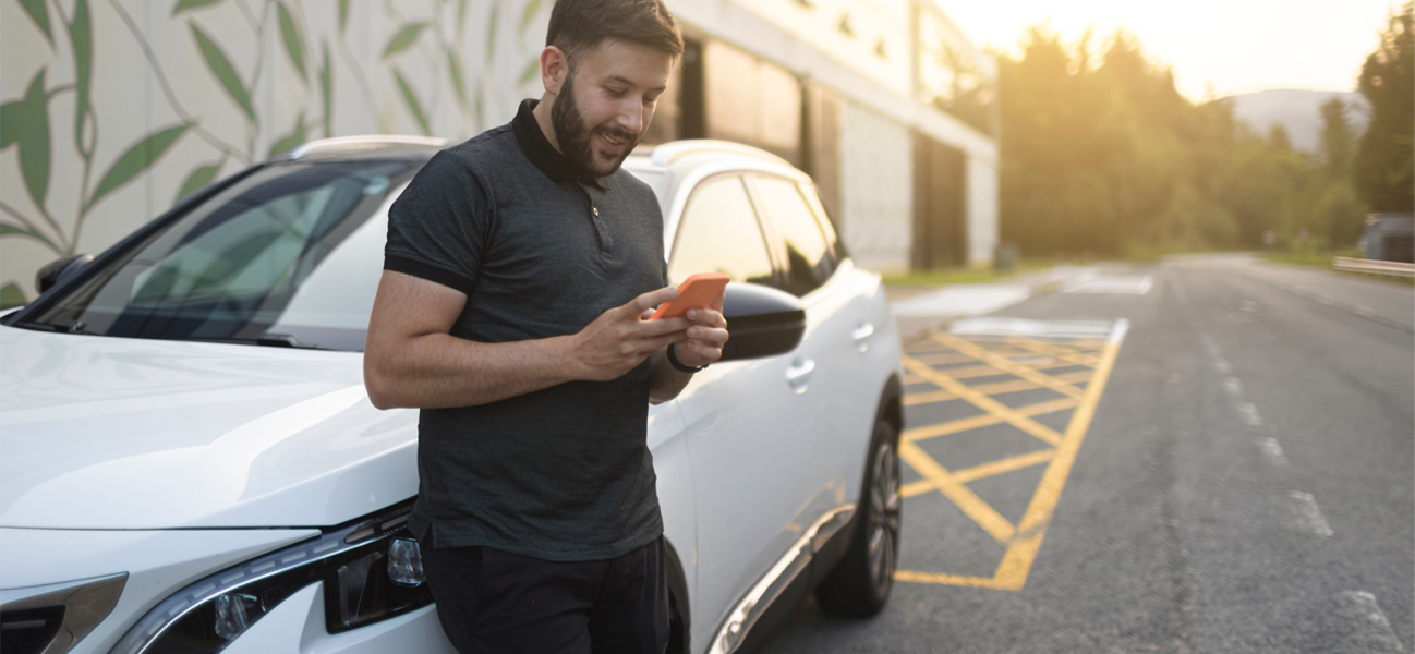 man leunt op auto met mobiel in hand