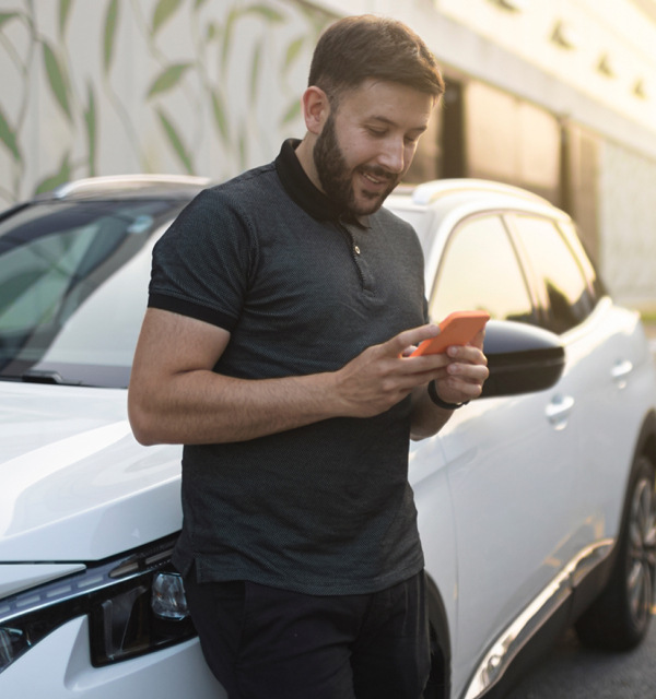 man leunt op auto met mobiel in hand
